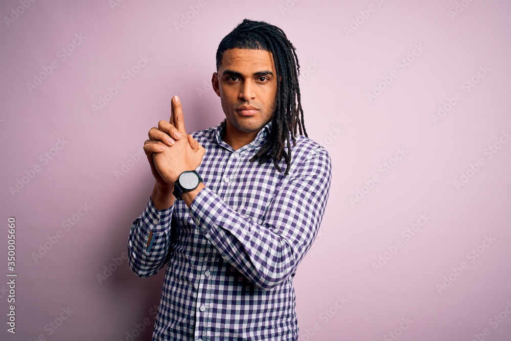 Young handsome african american afro man with dreadlocks wearing casual shirt Holding symbolic gun with hand gesture, playing killing shooting weapons, angry face