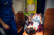 © Anna Kosolapova - A paramedic stands over the unconscious woman lying on a stretcher in an ambulance car, a little girl sitting beside her, holding her hand and crying