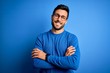 © Krakenimages.com - Young handsome man with beard wearing casual sweater and glasses over blue background happy face smiling with crossed arms looking at the camera. Positive person.