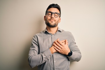 Sticker - Young handsome man wearing elegant shirt and glasses over isolated white background smiling with hands on chest with closed eyes and grateful gesture on face. Health concept.