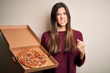 Poster - Young beautiful girl holding delivery box with Italian pizza standing over white background annoyed and frustrated shouting with anger, crazy and yelling with raised hand, anger concept