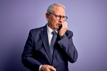 Poster - Grey haired senior business man wearing glasses and elegant suit and tie over purple background looking stressed and nervous with hands on mouth biting nails. Anxiety problem.