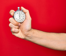 Wall Mural - Beautiful hand of man holding stopwatch doing countdown over isolated red background