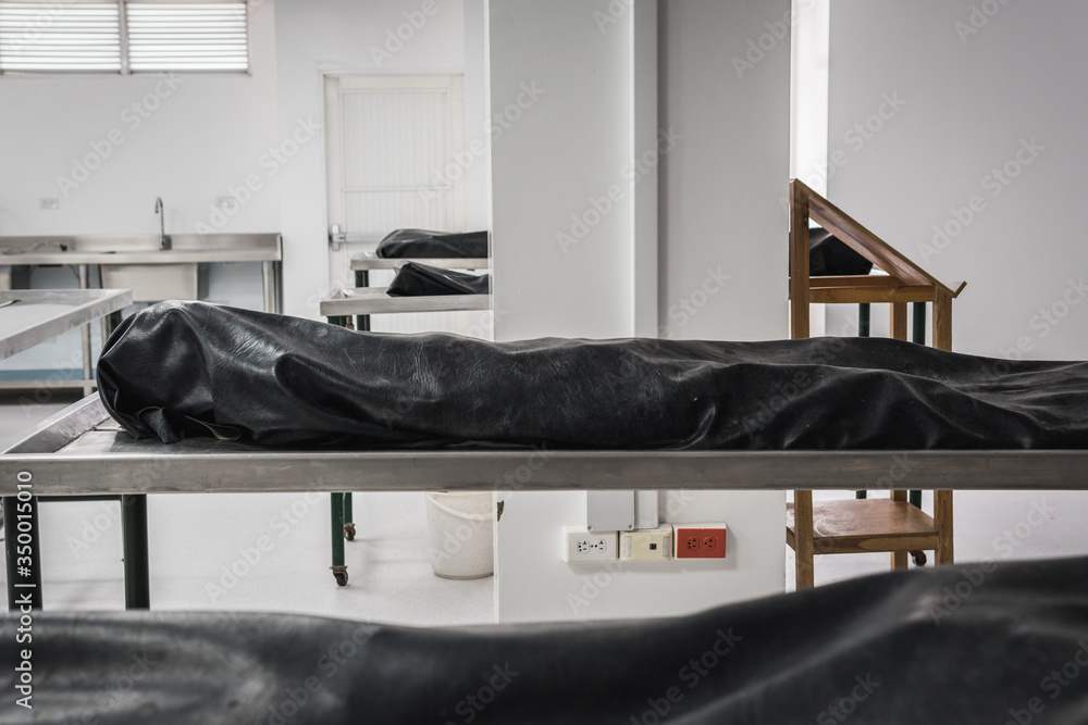 Covered human corpses on tables in a morgue / mortuary waiting for