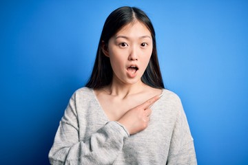 Sticker - Young beautiful asian woman wearing casual sweater standing over blue isolated background Surprised pointing with finger to the side, open mouth amazed expression.