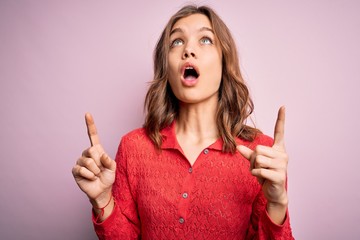 Young beautiful blonde casual girl over pink isolated background amazed and surprised looking up and pointing with fingers and raised arms.