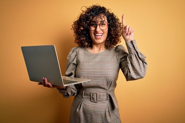 Poster - Beautiful arab businesswoman wearing glasses working using laptop over yellow background surprised with an idea or question pointing finger with happy face, number one