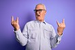 © Krakenimages.com - Middle age handsome hoary man wearing striped shirt and glasses over purple background shouting with crazy expression doing rock symbol with hands up. Music star. Heavy concept.