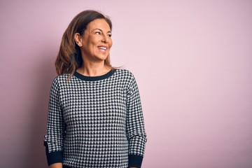 Poster - Middle age beautiful woman wearing casual sweater standing over isolated pink background looking away to side with smile on face, natural expression. Laughing confident.