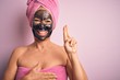 © Krakenimages.com - Middle age brunette woman wearing beauty black face mask over isolated pink background smiling swearing with hand on chest and fingers up, making a loyalty promise oath