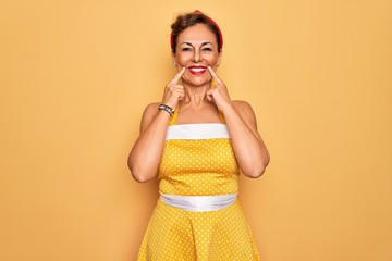 Sticker - Middle age senior pin up woman wearing 50s style retro dress over yellow background Smiling with open mouth, fingers pointing and forcing cheerful smile