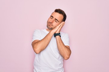 Handsome man with blue eyes wearing casual white t-shirt standing over pink background sleeping tired dreaming and posing with hands together while smiling with closed eyes.