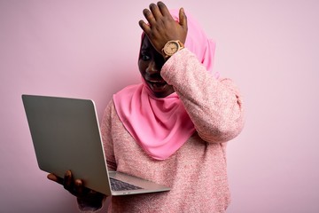 Poster - African american plus size woman wearing muslim hijab using laptop over pink background surprised with hand on head for mistake, remember error. Forgot, bad memory concept.