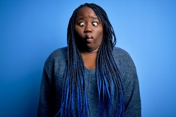 Sticker - African american plus size woman with braids wearing casual sweater over blue background making fish face with lips, crazy and comical gesture. Funny expression.