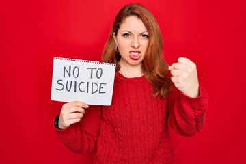 Sticker - Beautiful redhead woman holding banner showing no to suicide message over red background annoyed and frustrated shouting with anger, crazy and yelling with raised hand, anger concept