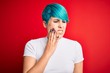 © Krakenimages.com - Young beautiful woman with blue fashion hair wearing casual t-shirt over red background touching mouth with hand with painful expression because of toothache or dental illness on teeth. Dentist