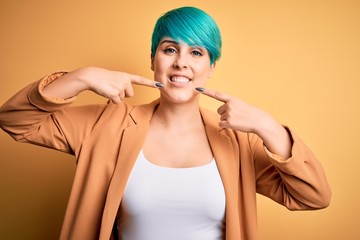 Sticker - Young beautiful woman with blue fashion hair wearing casual jacket over yellow background smiling cheerful showing and pointing with fingers teeth and mouth. Dental health concept.