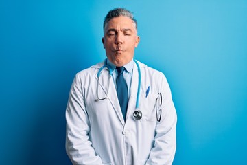 Poster - Middle age handsome grey-haired doctor man wearing coat and blue stethoscope making fish face with lips, crazy and comical gesture. Funny expression.