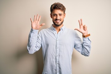 Young handsome man with beard wearing striped shirt standing over white background showing and pointing up with fingers number eight while smiling confident and happy.