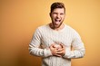 © Krakenimages.com - Young blond man with beard and blue eyes wearing white sweater over yellow background smiling and laughing hard out loud because funny crazy joke with hands on body.