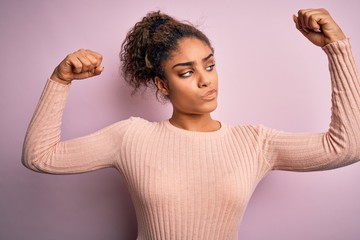 Sticker - Young beautiful african american girl wearing casual sweater standing over pink background showing arms muscles smiling proud. Fitness concept.