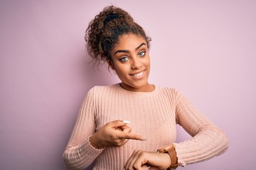 Poster - Young beautiful african american girl wearing casual sweater standing over pink background In hurry pointing to watch time, impatience, upset and angry for deadline delay