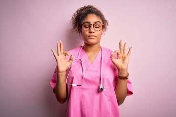 Poster - African american nurse girl wearing medical uniform and stethoscope over pink background relax and smiling with eyes closed doing meditation gesture with fingers. Yoga concept.