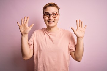 Wall Mural - Young handsome redhead man wearing casual t-shirt standing over isolated pink background showing and pointing up with fingers number ten while smiling confident and happy.