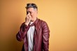 © Krakenimages.com - Young handsome modern man wearing fashion leather jacket and sunglasses over yellow background smelling something stinky and disgusting, intolerable smell, holding breath with fingers on nose