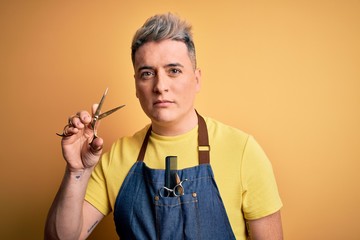 young modern professional hairdresser man holding scissors over isolated yellow background with a co