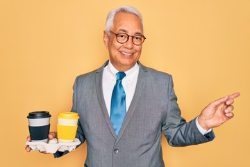 Sticker - Middle age senior grey-haired business man wearing glasses holding coffee cup on tray very happy pointing with hand and finger to the side