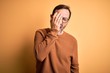 © Krakenimages.com - Middle age hoary man wearing brown sweater and glasses over isolated yellow background Yawning tired covering half face, eye and mouth with hand. Face hurts in pain.