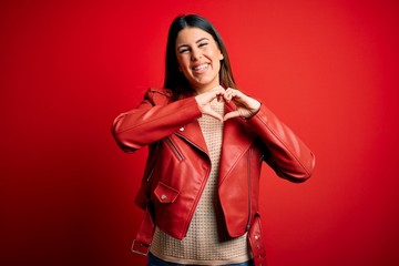 Canvas Print - Young beautiful woman wearing red leather jacket over isolated background smiling in love showing heart symbol and shape with hands. Romantic concept.