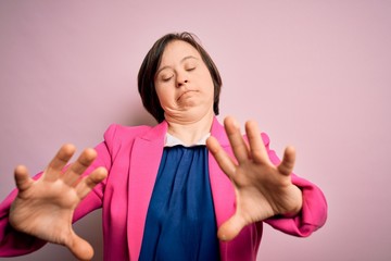 Sticker - Young down syndrome business woman over pink background afraid and terrified with fear expression stop gesture with hands, shouting in shock. Panic concept.