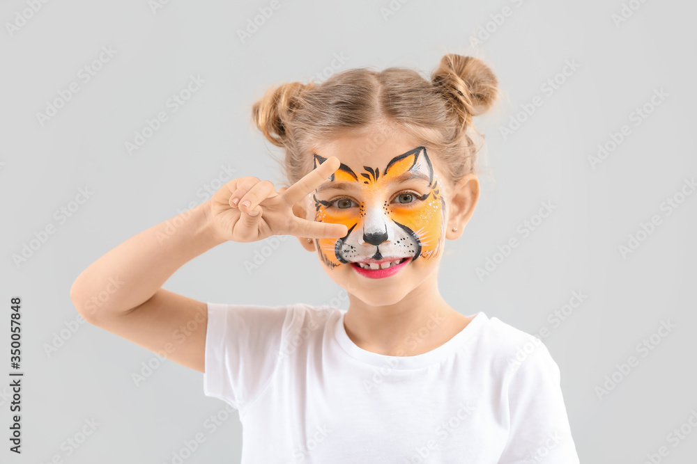Funny little girl with face painting on light background