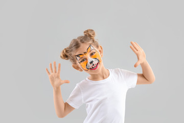 Funny little girl with face painting on light background