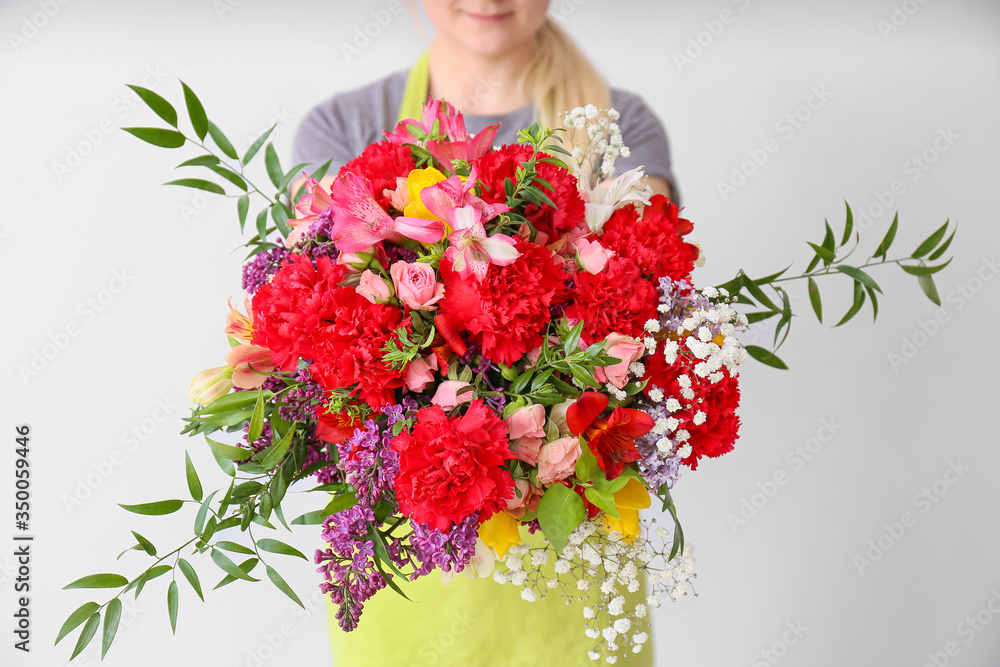Female florist with beautiful bouquet on light background
