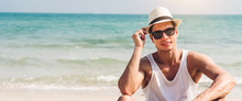 Portrait Of Smiling Happy Handsome Man Model Enjoying And Relax In Fashionable Sunglasses And Hipster Summer Straw Hat Standing On The Tropical Beach And Looking At Camara.Summer Vacations And Travel