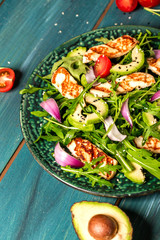 Fresh salad plate with arugula, halloumi cheese, tomatoes and avocado wooden background close up. Healthy food. Green meal