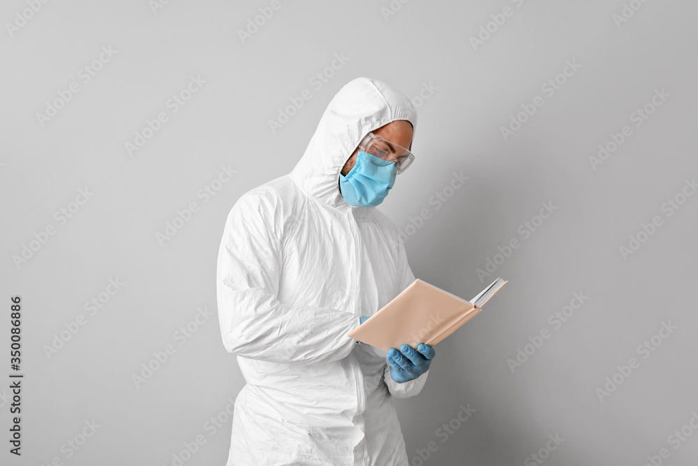 Man in biohazard suit reading book on grey background