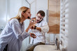 © Dusan Petkovic - Handsome caucasian couple standing in bathroom and preparing for work. Man talking on the smart phone and looking at wristwatch while woman standing in front of mirror and putting powder.