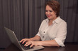 © galika - Smiling woman in white shirt working online at home. Female with laptop