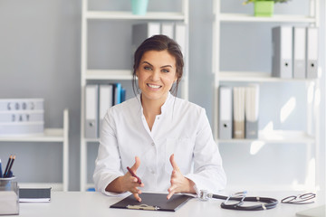 Smiling female doctor gives consultation at a table in a clinic office.