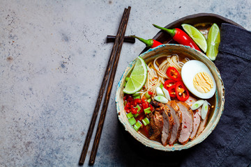 Wall Mural - Asian spicy ramen noodles with pork, egg and vegetables in blue bowl, gray background, top view.