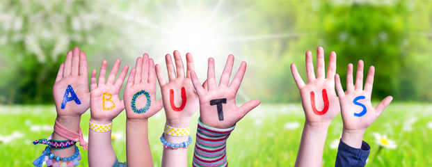 Wall Mural - Children Hands Building Colorful English Word About Us. Sunny Green Grass Meadow As Background