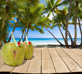 Canvas Print - Wooden tabletop with coconut drinks and place for Your product advertisement. Tropical beach in the background. Summer holiday concept