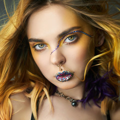 Woman with creative yellow coloring hair and makeup with rhinestones, purple strands of hair second layer. Bright color curly hair on the girl's head, professional makeup