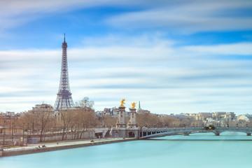 Wall Mural - Beautiful cityscape of the river Seine with the Pont Alexandre III bridge and the Eiffel tower in Paris, France, with clouds in spring