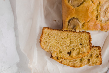 Wall Mural - Homemade sliced healthy banana bread ready for serve on breakfast on the white concrete background with craft baking paper and pastry knife. Top view. Close up shoot