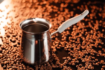 Freshly brewed coffee in cezve on a dark golden background next to scattered roasted coffee beans.